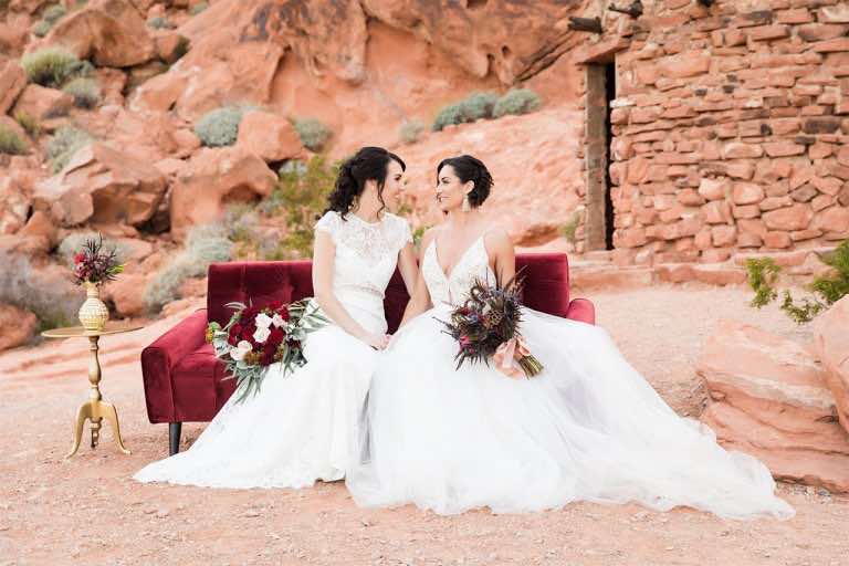 Young newlyweds in wedding dresses sitting outside on a red couch