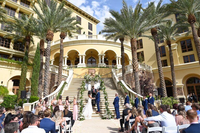 An outdoor wedding venue filled with guests and palm trees in the background