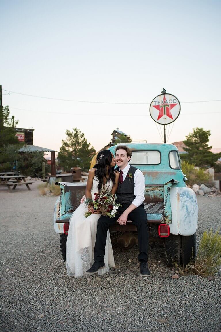 A bride and groom sitting in the back of an old pickup truck