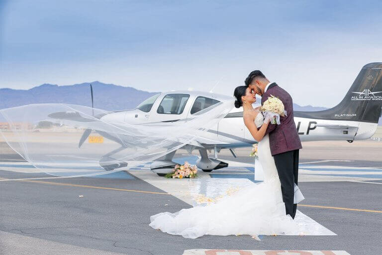 Newlyweds pose on a runway in front of a small airplane