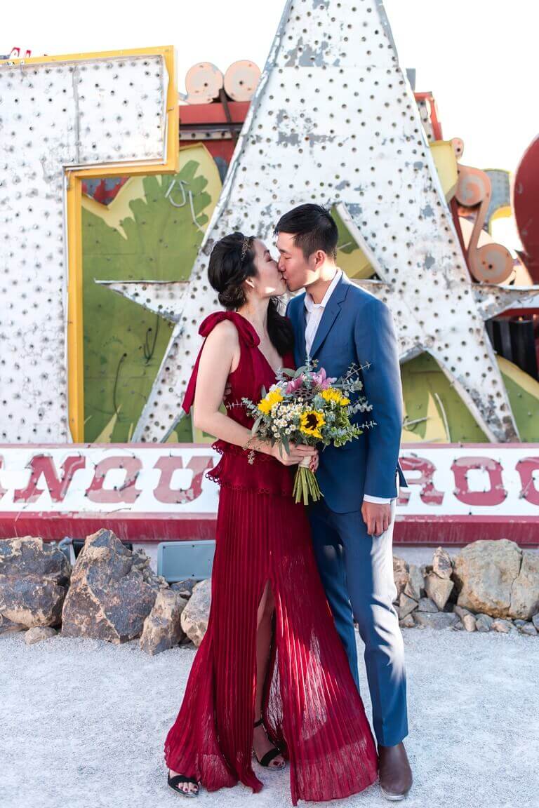 A bride and groom kissing on their wedding day in front of The Neon Museum