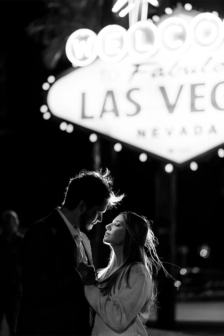 An intimiate couple standing in front of the Welcome to Las Vegas sign at night