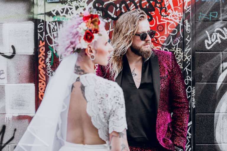 A tattooed bride and groom standing in front of graffiti art
