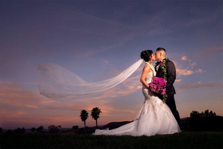 A wedding couple kissing at dusk with palm trees in the background