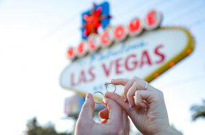 Couple holding up wedding rings in front of Welcome to Las Vegas Sign