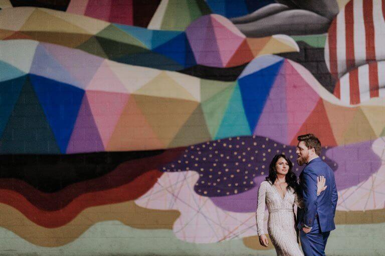 A young couple poses in front of a brightly painted wall