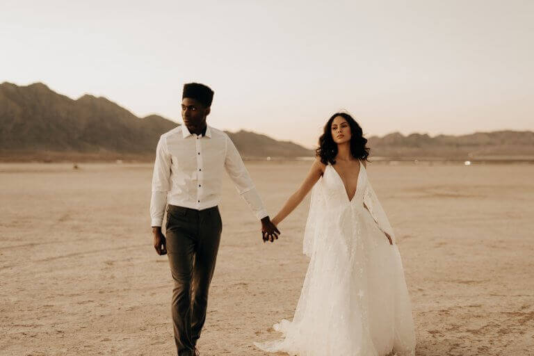 Newlyweds holding hands walking through the desert