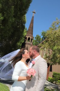 A bride and groom kiss in front of a church steeple