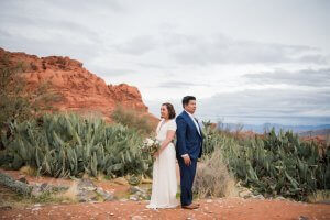 A bride and groom stand back-to-back in front of a desert backdrop