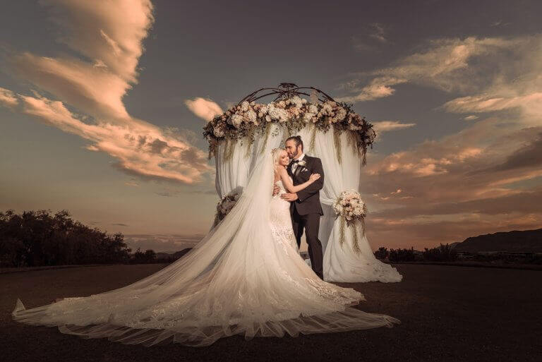 Wedding couple embracing in front of an arch at dusk