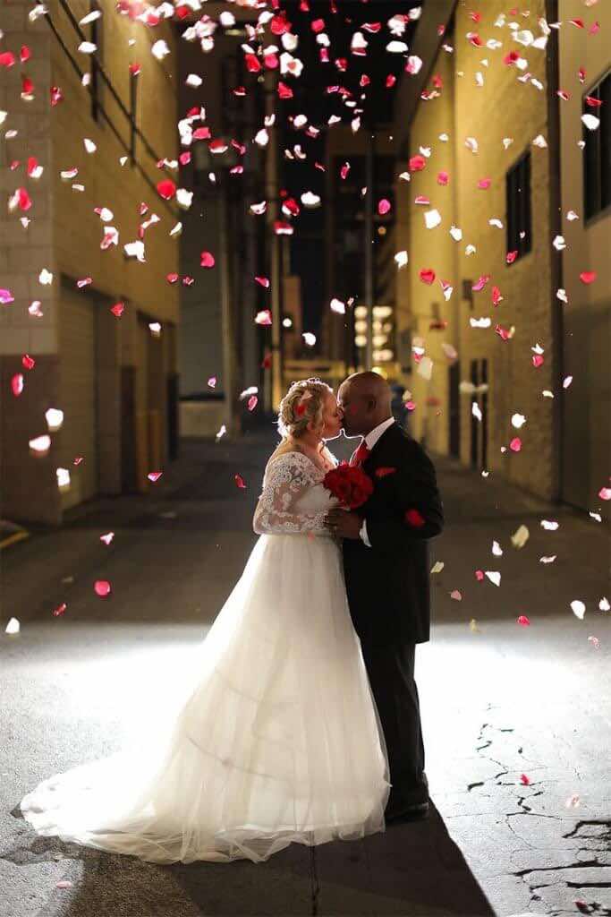 Newlyweds kissing outside at night surrounded by falling rose petals