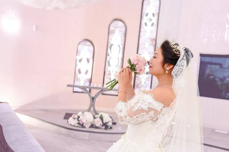 A bride smelling a pink rose bouquet inside a wedding chapel