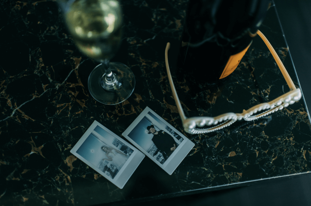 Vintage camera photos of the bride and groom with a champagne bottle and sunglasses on a marble table