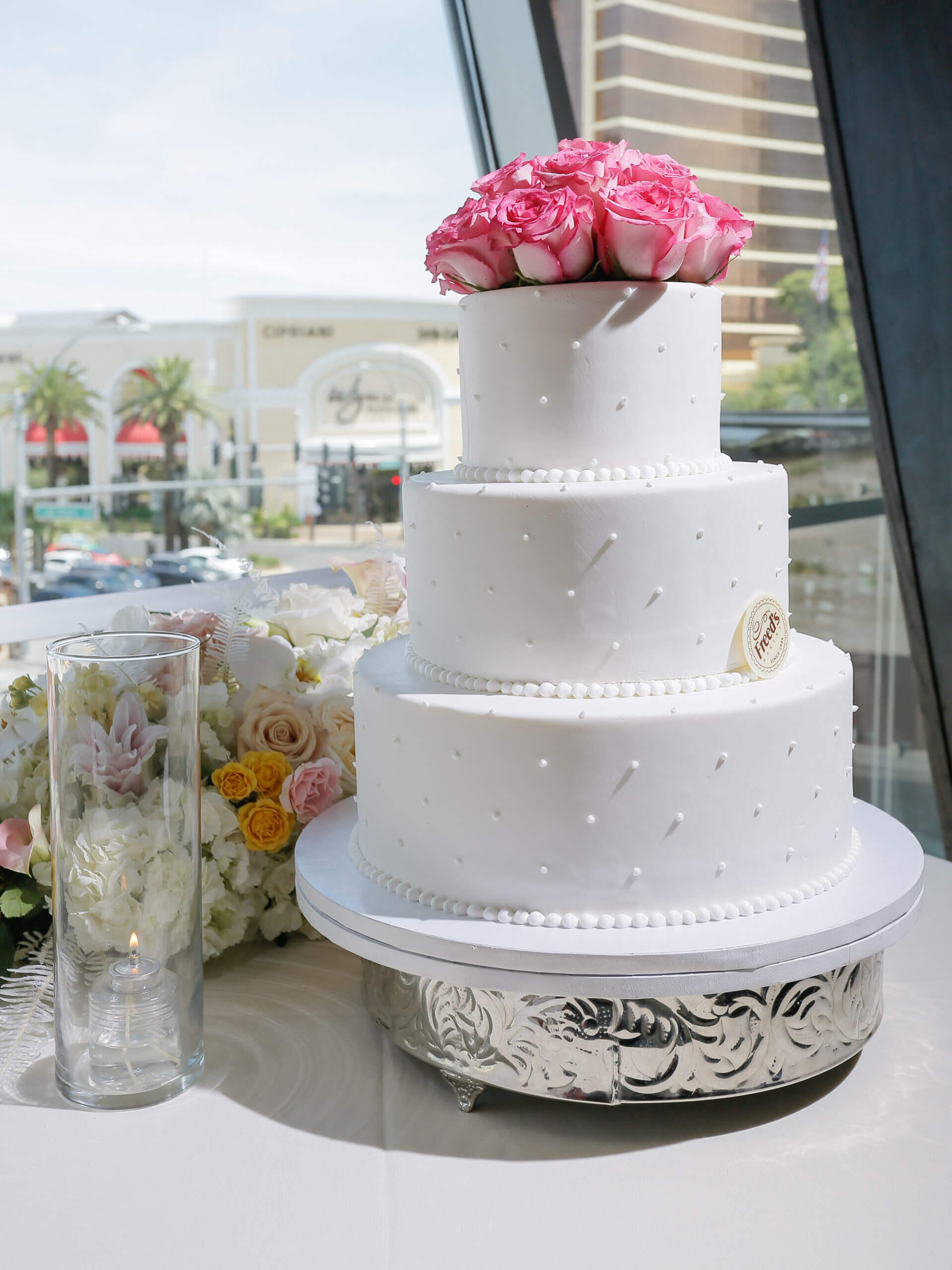 a white cake on a silver tray with pink roses