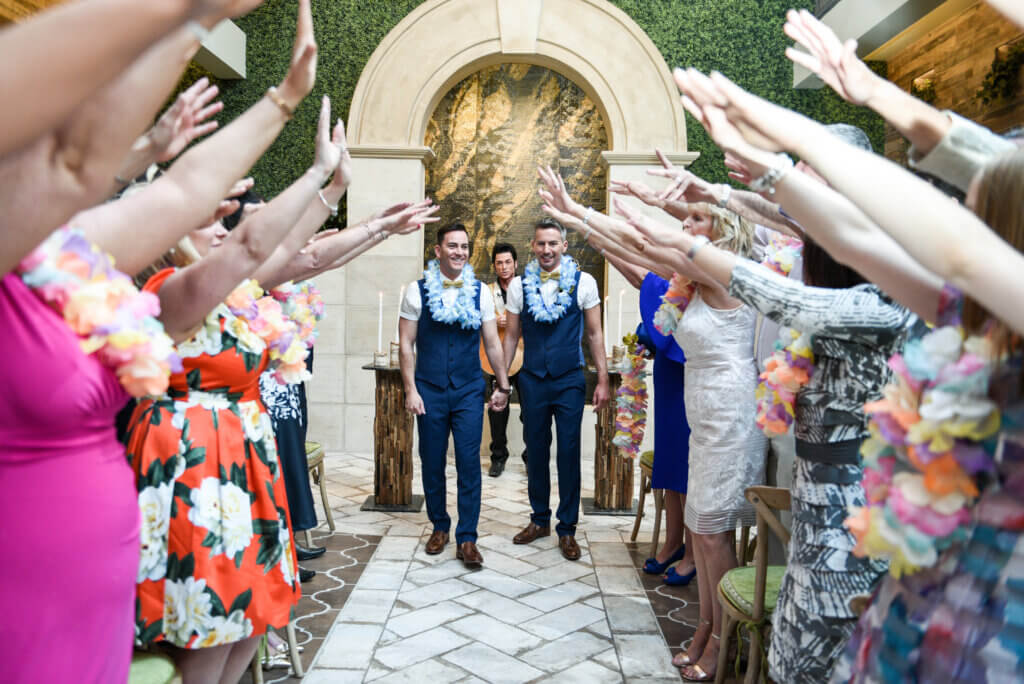 two grooms in leis walking down the aisle