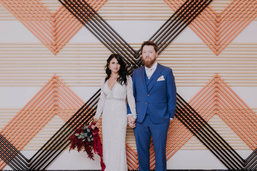 a couple stands in front of a geometric wall in fashionable clothing