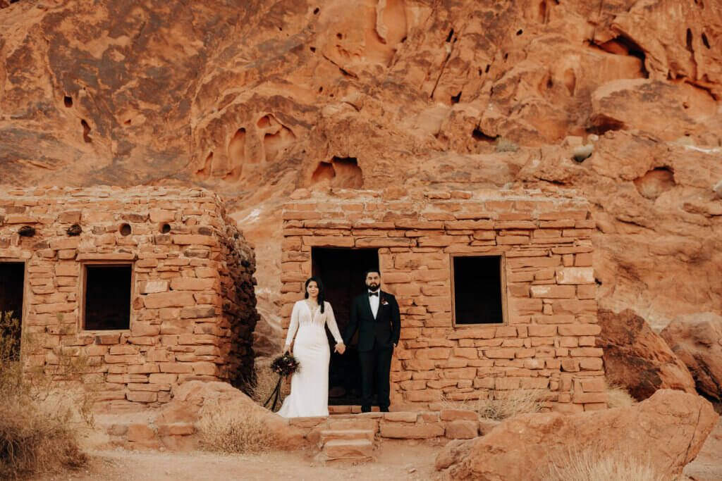 a couple standing in front of a stone building holding hands