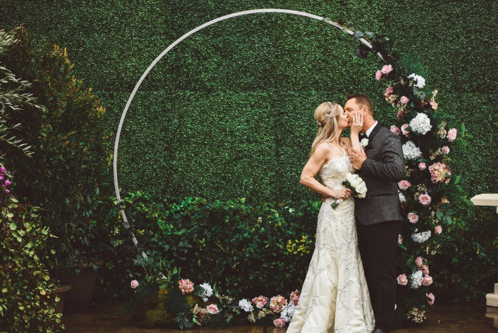 a wedding couple kissing in front of a floral hoop