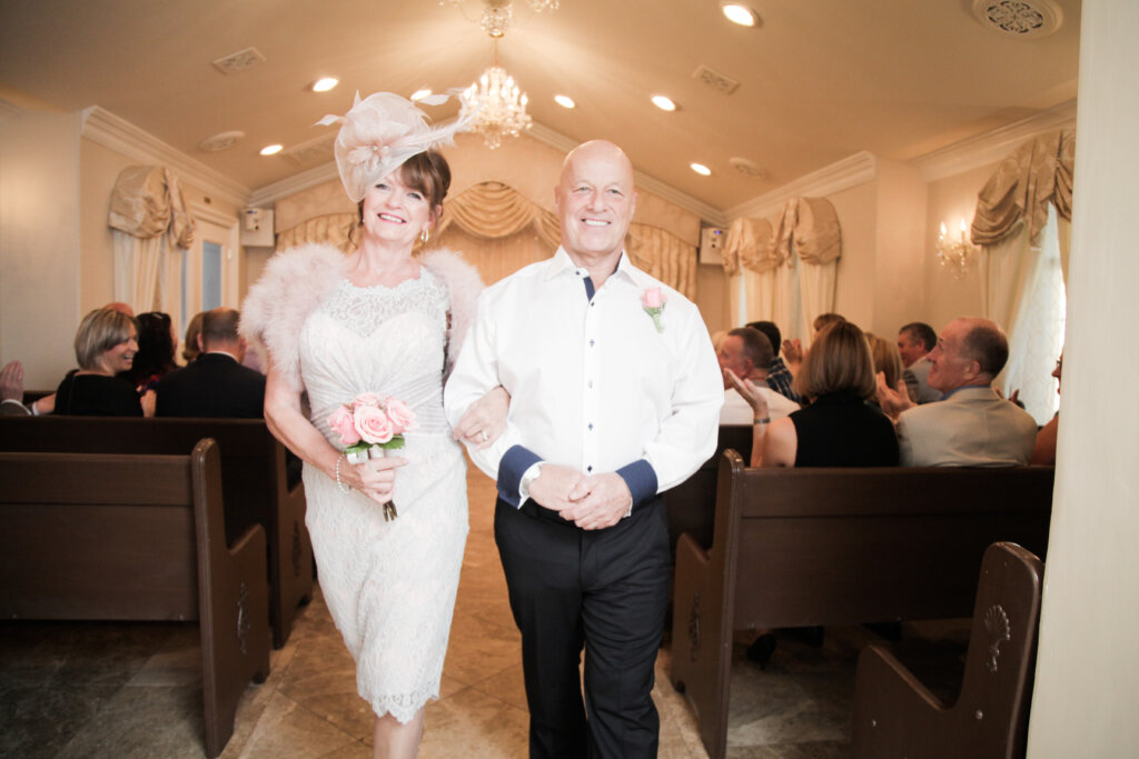 a woman in a fascinator and groom walking down a chapel aisle