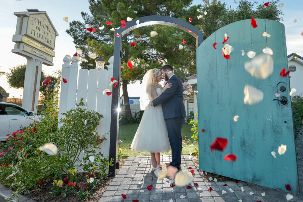 a wedding couple with rose petals in front of a blue gate