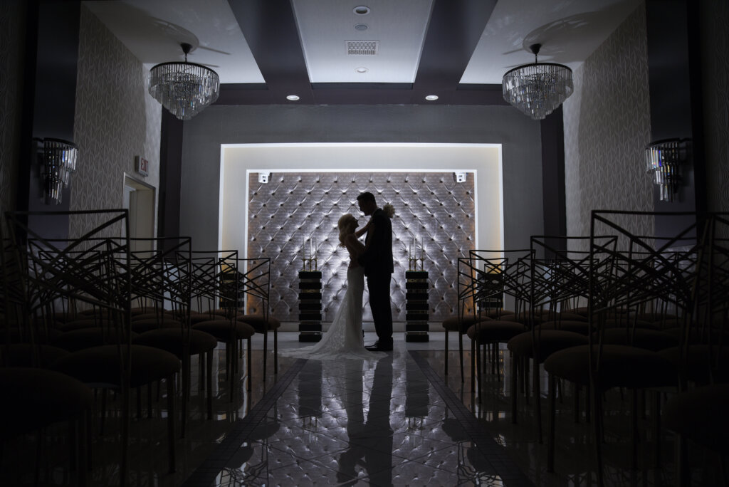 a dark wedding chapel with a white lit background and a couple embracing