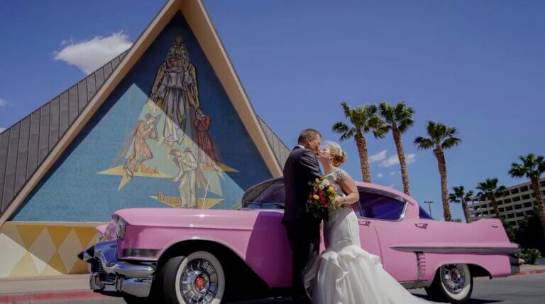 a wedding couple kissing in front of a pink Cadillac