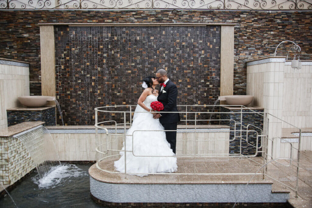 a wedding couple kissing near a water fixture