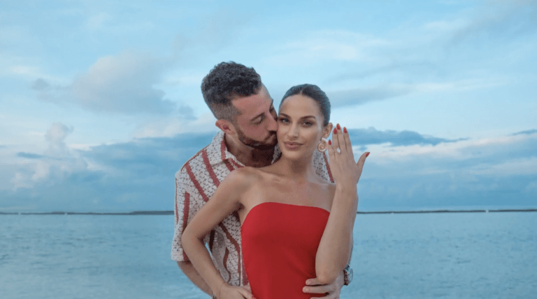 a woman holding up a wedding ring on the beach