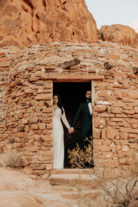 a wedding couple standing in a stone halfway hidden and holding hands
