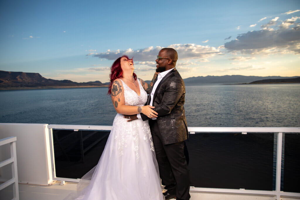a bride with tattoos and a groom with glasses laughing on a boat deck